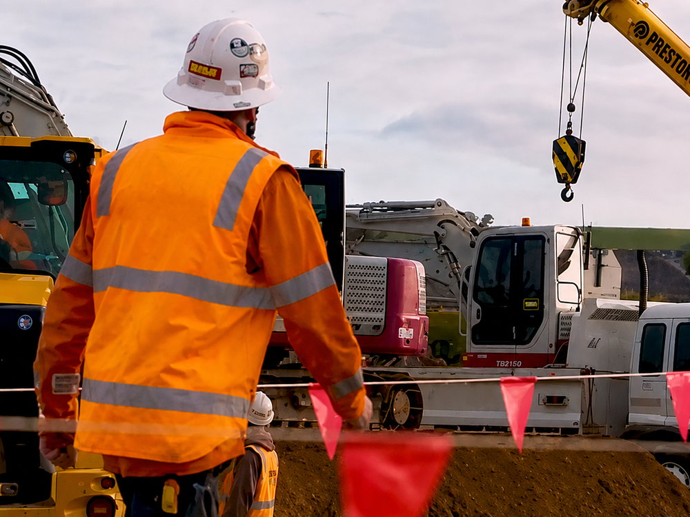 Site worker in high-visibility clothing directing plant during earthworks